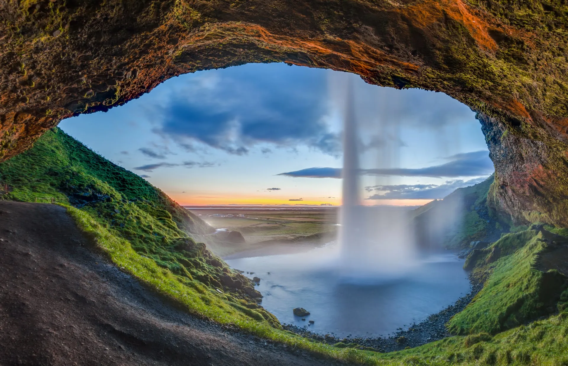 Seljalandsfoss waterfall falling from a green clifftop, with the walking path that leads behind the cascade on Iceland's South Coast