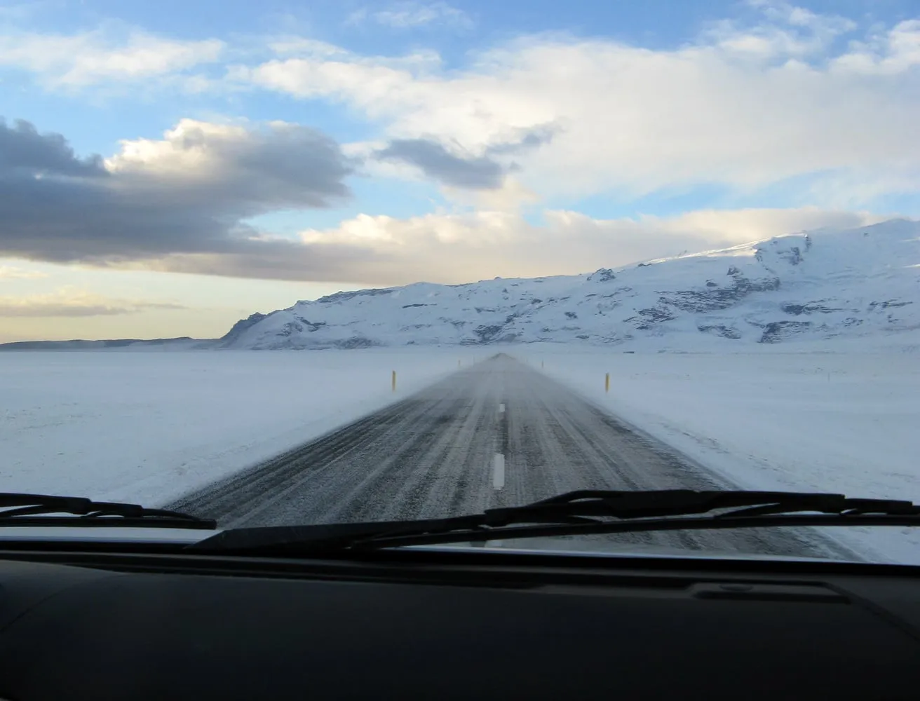 A snow- and ice-covered stretch of Iceland's Ring Road (Route 1) running through a flat winter landscape under an overcast sky