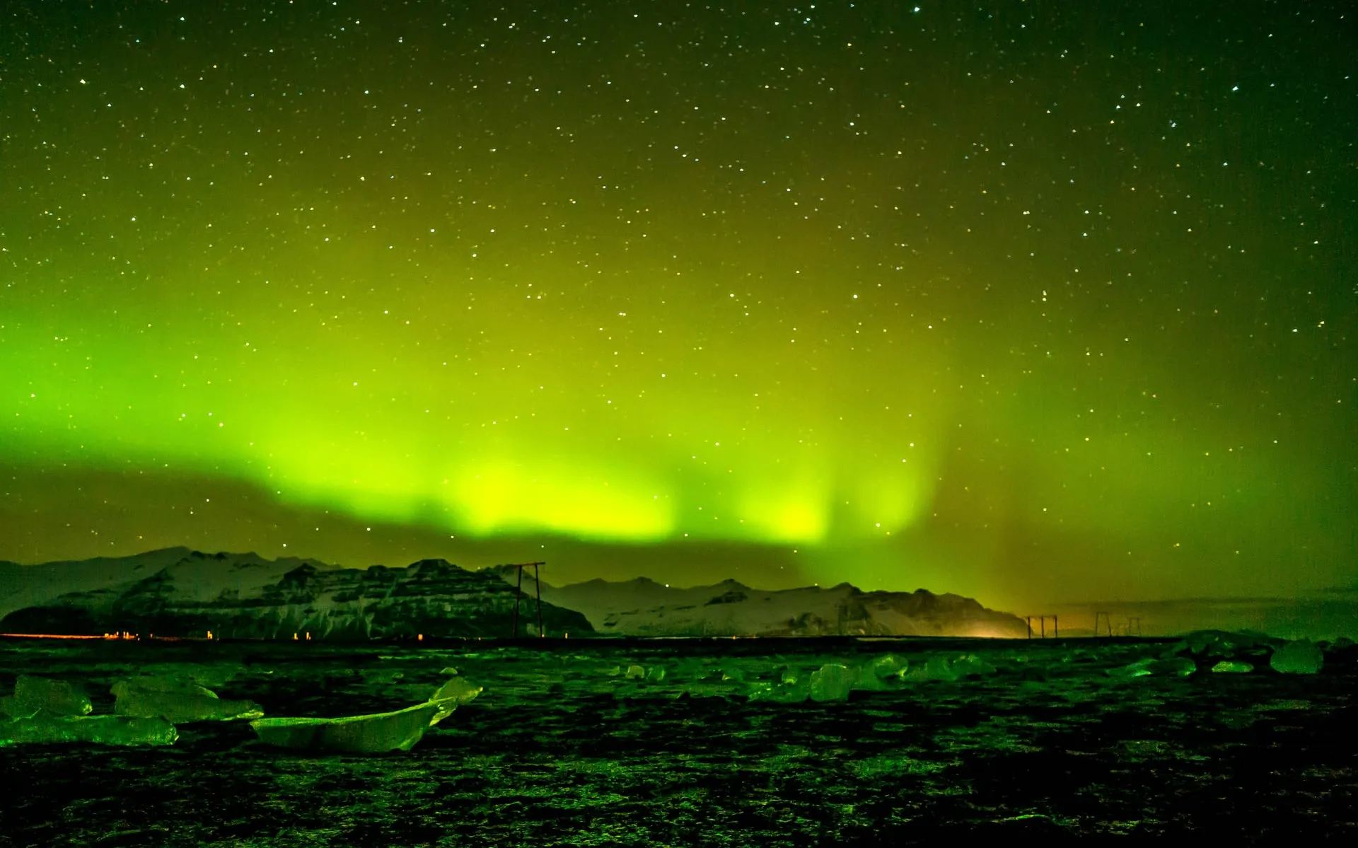 The northern lights glowing green over the ice-strewn Diamond Beach at Jökulsárlón during the late-winter aurora season