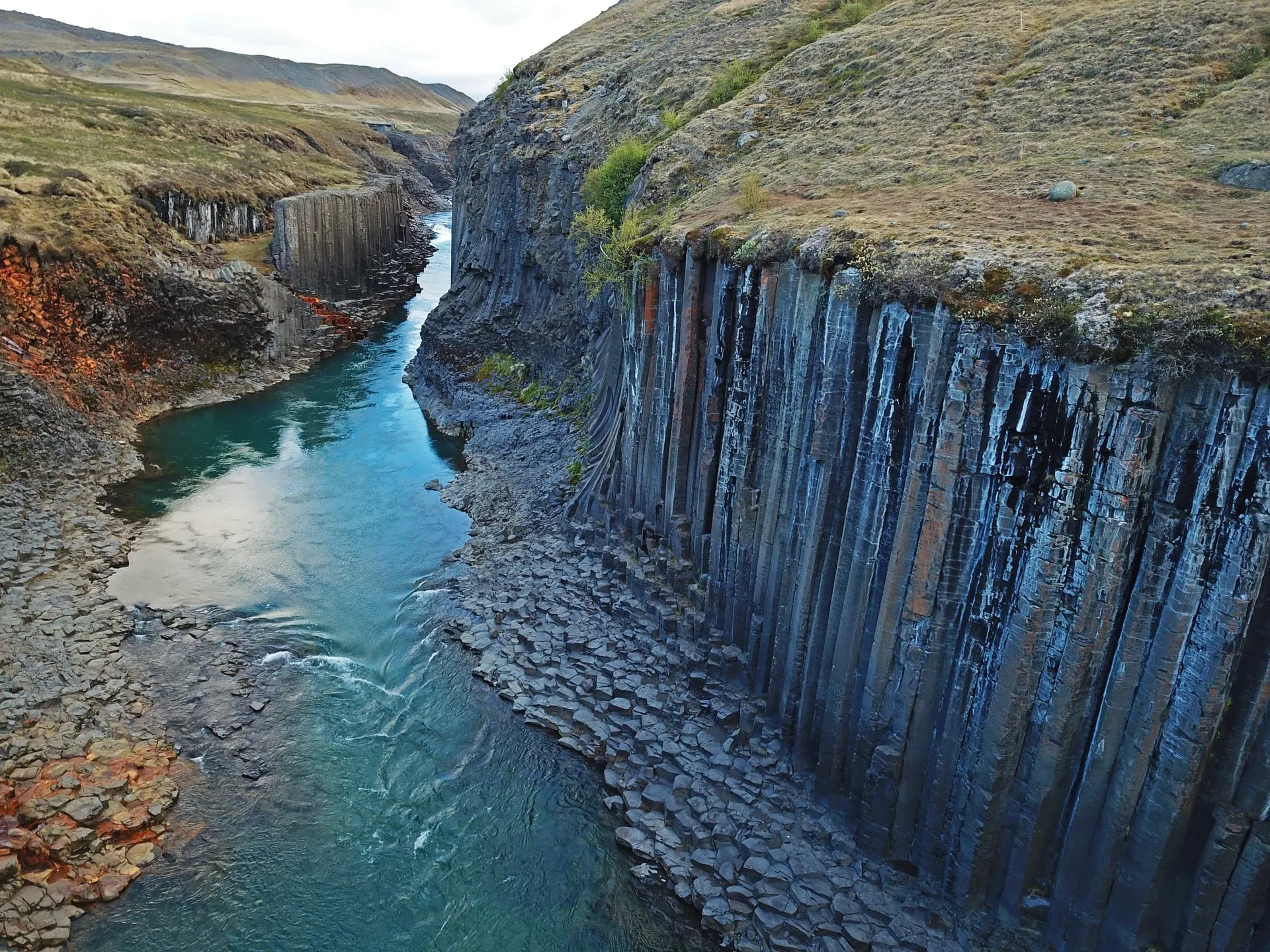 The blue-green glacial river of Stuðlagil canyon in East Iceland curving between towering walls of vertical basalt columns