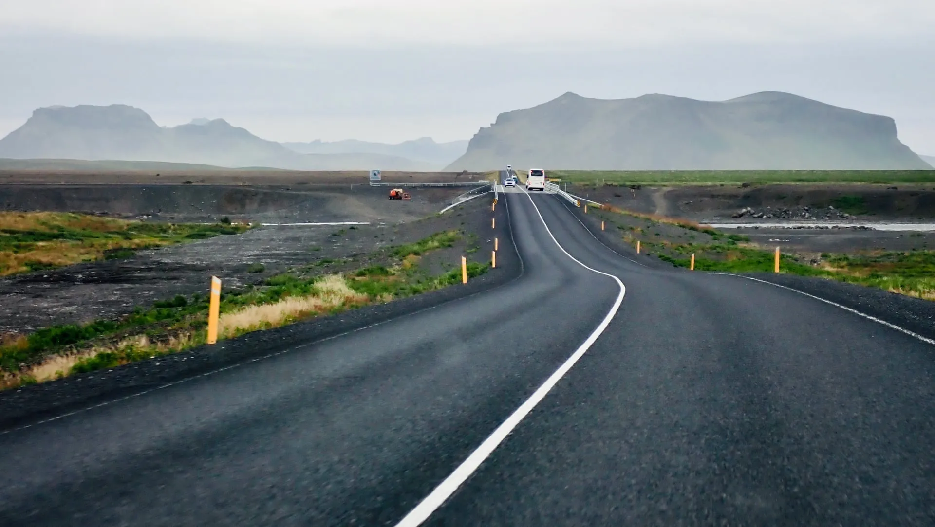 A wide road-view landscape of farmland and distant mountains in South Iceland