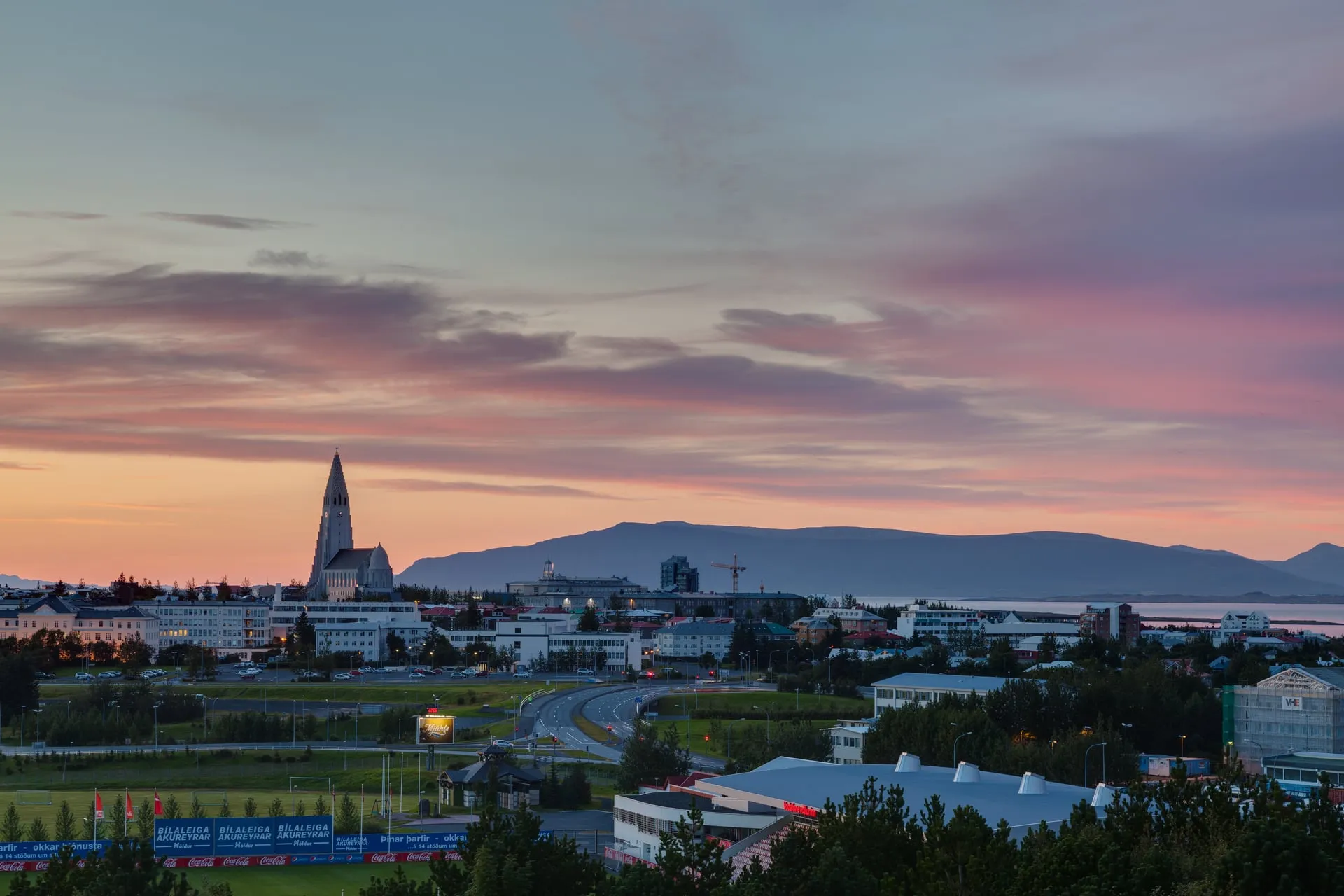 A panoramic cityscape of central Reykjavík seen from Perlan, with rooftops stretching to the sea and Hallgrímskirkja rising above the city