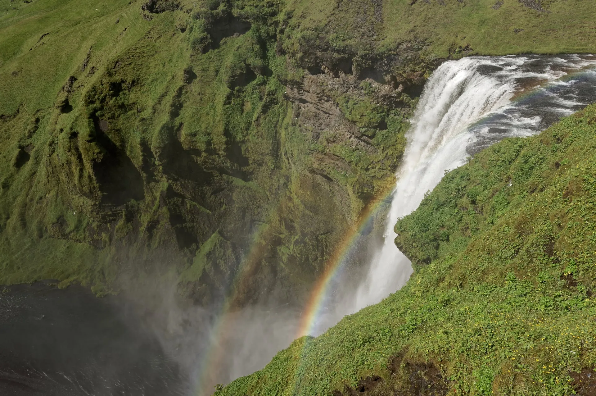 The Skógafoss waterfall pouring over a 60-metre cliff with a rainbow in its spray in South Iceland